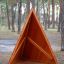 Փայտե խաղահրապարակի հատված Tipi Nature wooden house՝ եռանկյունաձև ձևով, ծառերի միջև կանգնած: