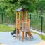 Pixie Modern Nature wooden playhouse with slide-y խոտապատ այգում եվ ցանկապատի մոտ գտնվող մանկական խա